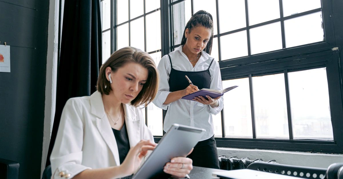 Two business professionals reviewing digital information on a tablet and taking notes in a contemporary office